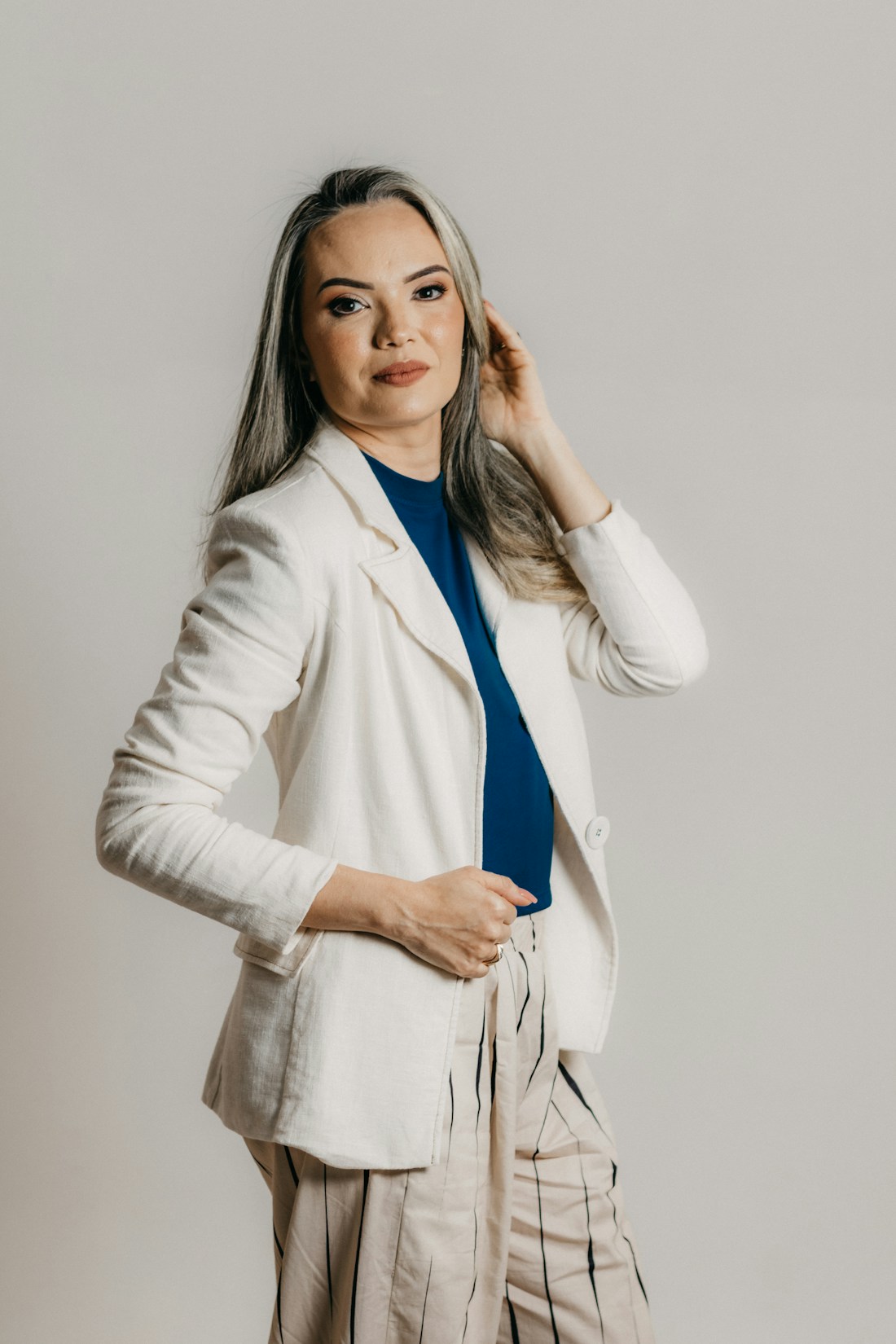 A woman wearing a white blazer over a blue top in a bright studio portrait