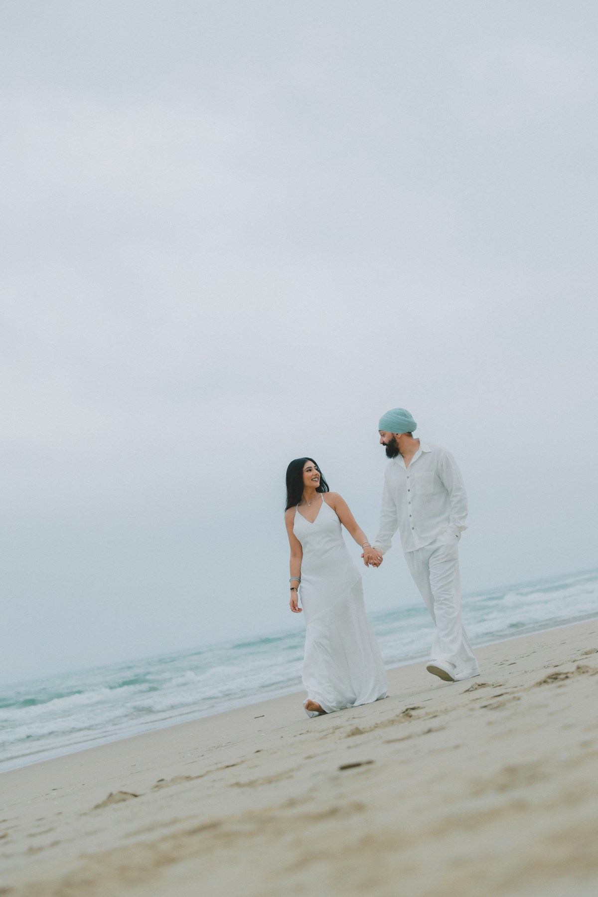 A couple in white walking hand in hand along the shoreline