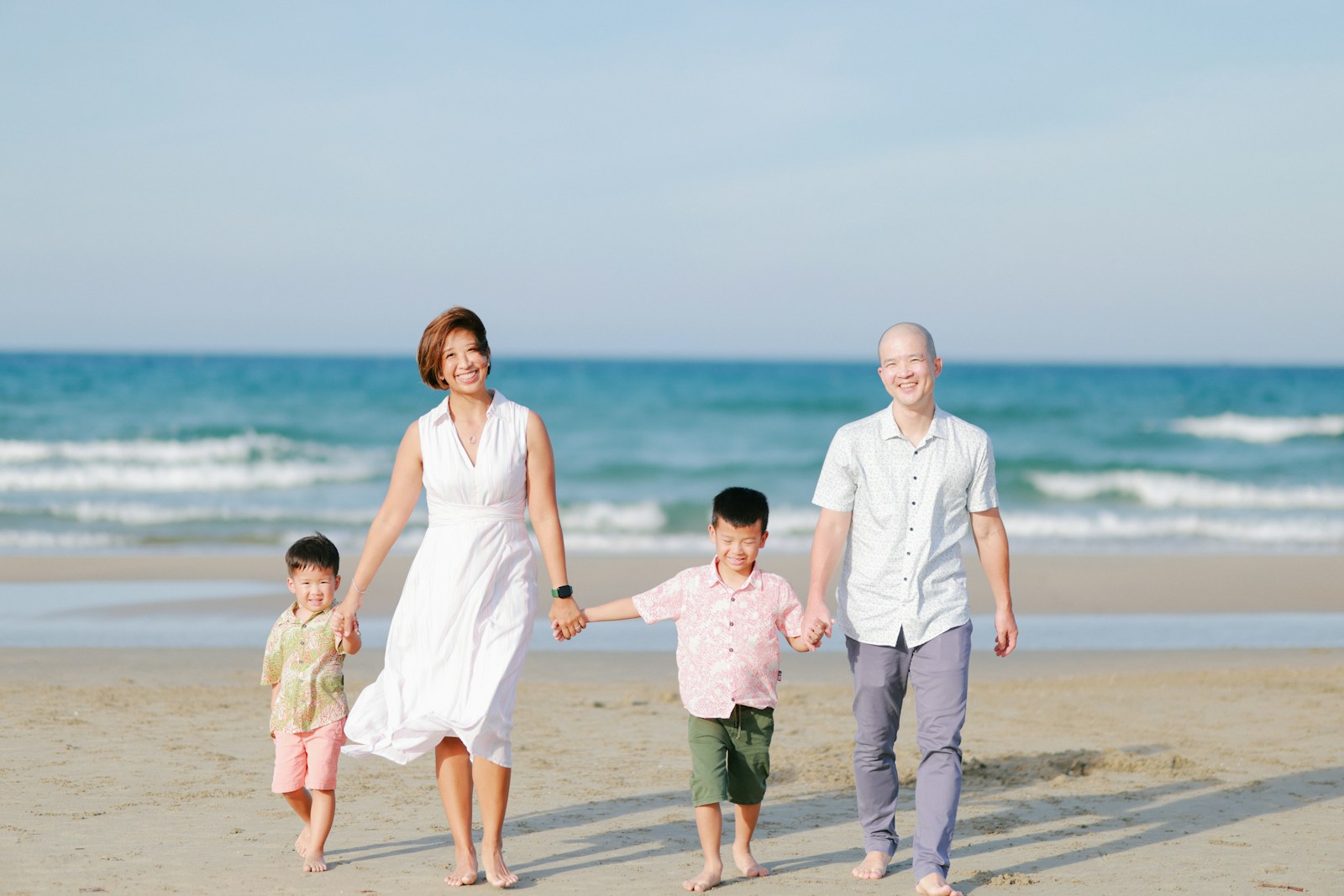 A family in light summer clothes walking together along the beach